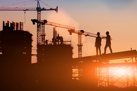construction workers on steel beam at sunrise with cranes in the background
